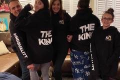 Family in matching black hoodies poses playfully at home, showcasing the backs with a "THE KING" print.