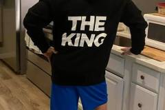 Person in hoodie with "THE KING" text, standing in a kitchen.