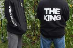 Two people standing outside, one facing away with "THE KING" on the back of his hoodie.