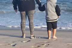 Two people holding hands on the beach, one wearing a hoodie labeled "THE KING".