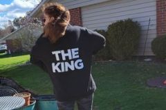 Person in a "THE KING" sweatshirt standing outside a house.