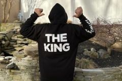 Person in a hoodie with "THE KING" back print flexing muscles outdoors.