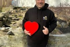 Man in hoodie holding a heart-shaped object outdoors with a KQ hoodie