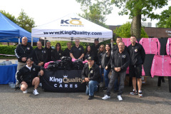 Group of people smiling under at an event under a tent with 'King Quality Cares' banner.