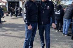 Two men smiling and standing together outdoors.