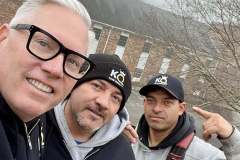 Three men posing for a selfie with foggy background and a brick building.