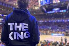 Person in 'THE KING' hoodie watching a basketball game.