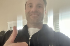 Man in a black branded jacket giving a thumbs up.