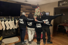 Four people in 'THE KING' hoodies posing in front of a Christmas tree.