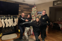 Four people posing with Christmas tree and festive decor, smiling and playful.