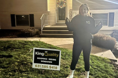 Person standing next to a "King Quality" sign at night outside a house.