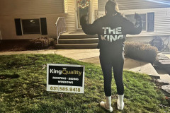 Person in a hoodie standing by a 'King Quality' sign in front of a house at night.