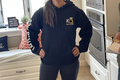 Woman in a black hoodie and leggings standing in a kitchen.