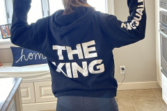 Person in hoodie with "THE KING" text, standing backwards in a kitchen