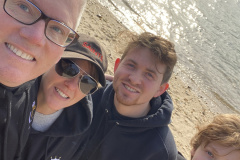 Four people in matching hoodies taking a selfie by the beach.