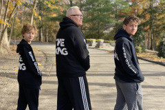 Three people in matching hoodies with text, standing outside.