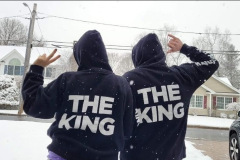 Two people with "THE KING" hoodies gesturing peace signs in the snow.