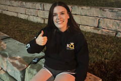 Woman sitting on a stone bench at night, giving a thumbs-up.