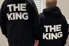 Two people from behind wearing matching "THE KING" hoodies, holding hands.