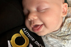 Sleeping baby resting on a shoulder with part of a logo visible.