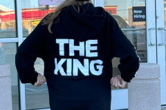 Person in black beanie and hoodie with "THE KING" text standing in front of a door.