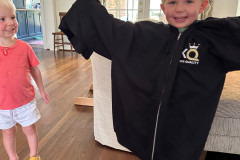 Two children playing, one wearing an oversized KQ jacket, smiling indoors.