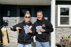 Two people smiling with blue branded socks  in front of a house.