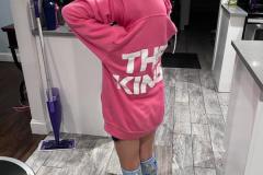 Child in a pink KQ hoodie and blue branded socks standing in a kitchen