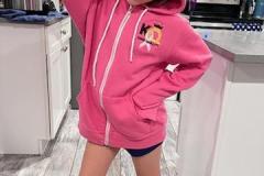 Child in a pink KQ hoodie and blue branded socks standing in a kitchen.