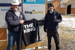 Two people posing with a "THE KING" sweatshirt at a construction site.