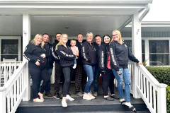 A group of people wearing matching hoodies posing on a house porch.