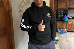 Man in black hoodie giving thumbs up in a kitchen.