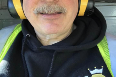 Man with mustache, glasses, and ear protection smiling at the camera.