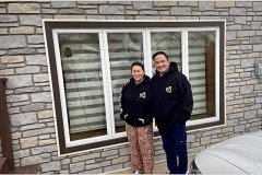 Two smiling people in matching jackets standing in front of a window.
