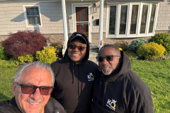 Three people in hoodies smiling in front of a house.