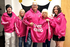 Group of five people wearing pink hoodies, one holding a hoodie with "THE KING" text.